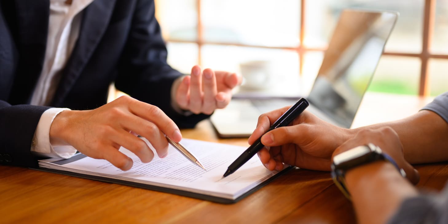 Closeup of an insurance agent pointing at a contract showing a client holding a pen where to sign.
