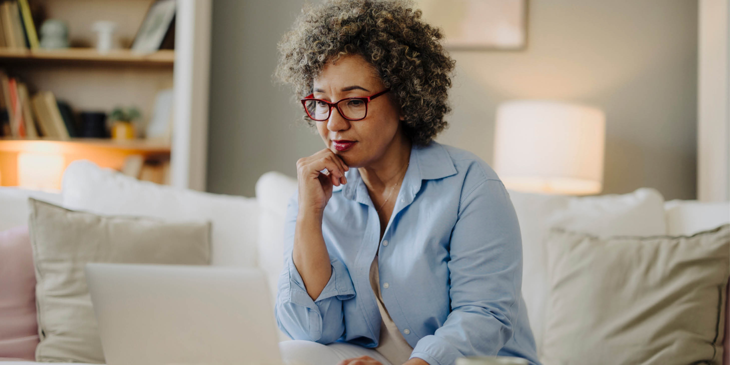 A woman focuses on a laptop screen while sitting on a couch