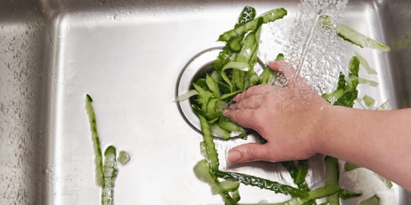woman washing green vegetables and putting skins down garbage disposal
