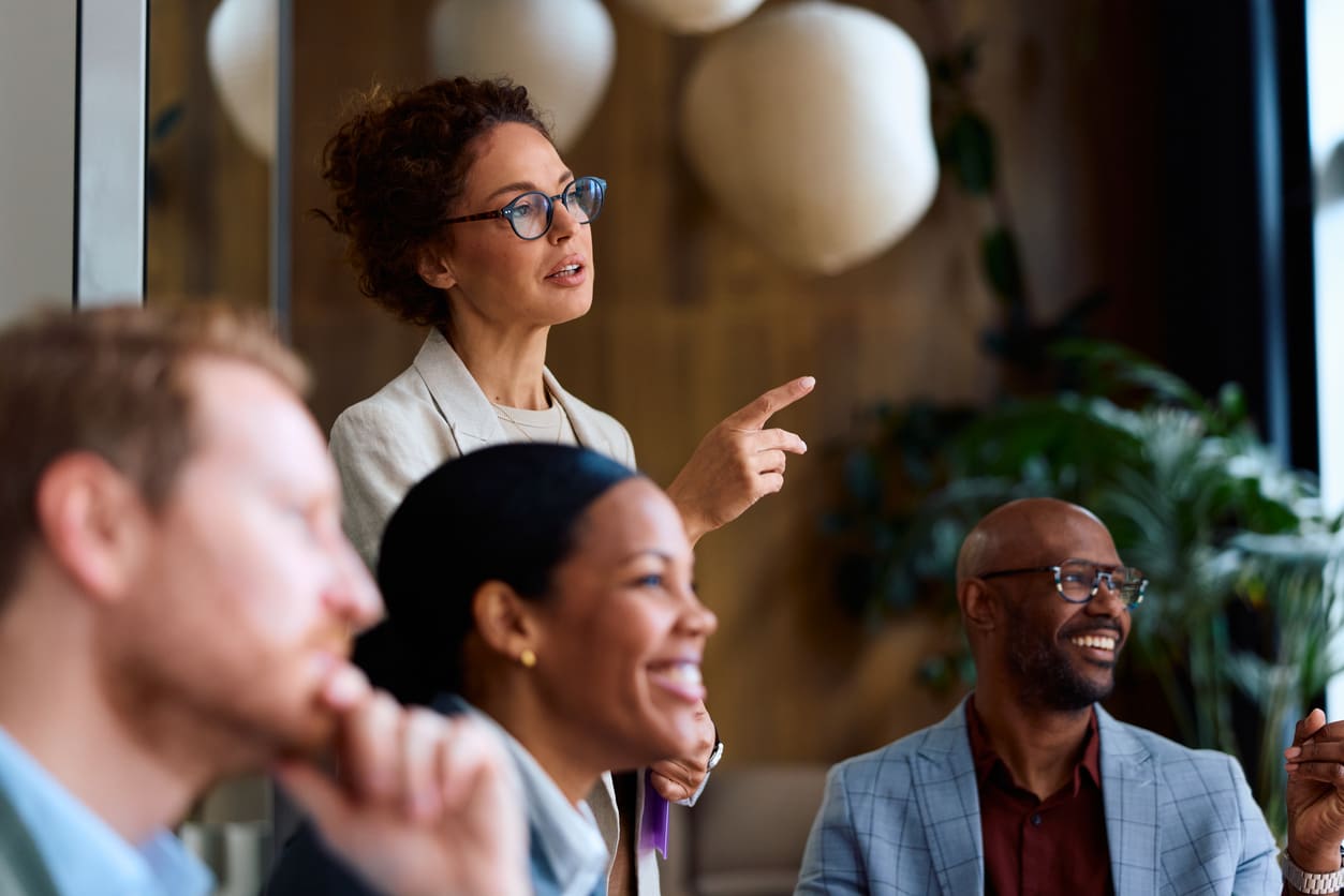 Businesswoman pointing ahead while surrounded by colleagues in a meeting.