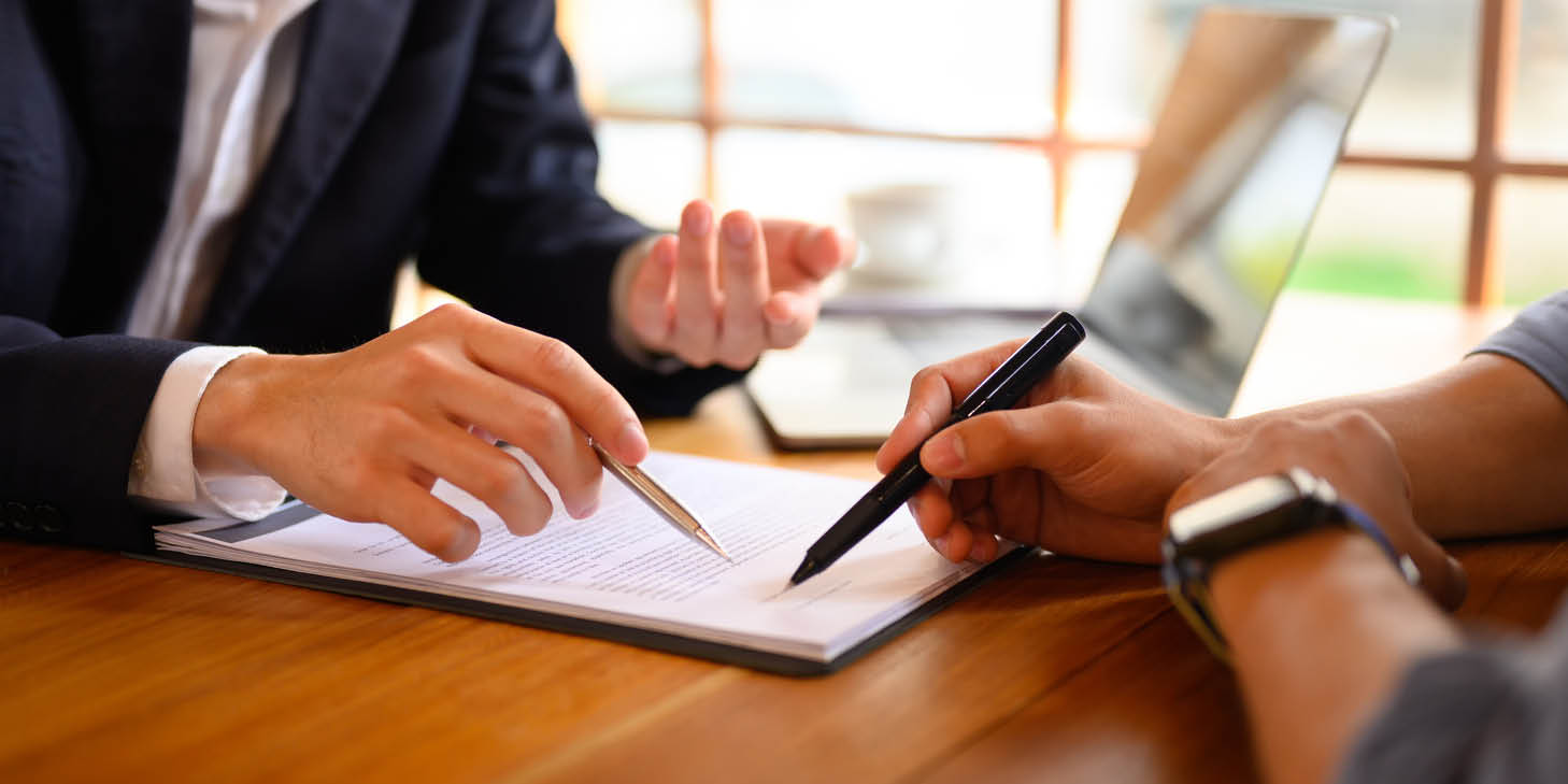 Insurance agent pointing at a contract showing a male client where to sign.