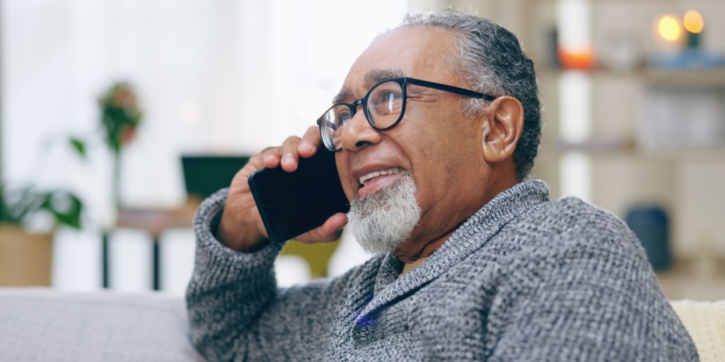 Older man smiling while sitting on a couch and talking on a cell phone