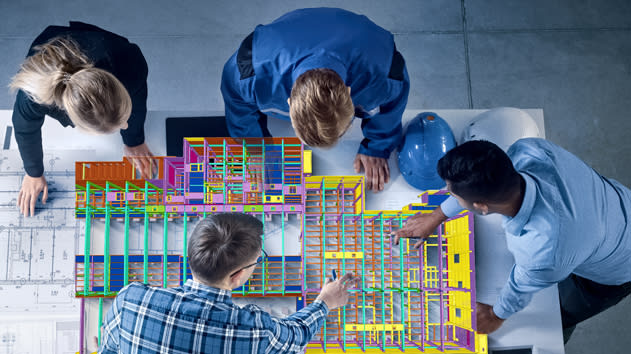Top-down view of four professionals gathered around a table, collaborating on a colorful 3D Building Information Modeling (BIM) structure displayed on a screen or printout, with architectural blueprints.