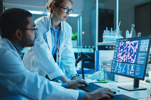 2 researchers in a laboratory reviewing genomics information on a computer screen.