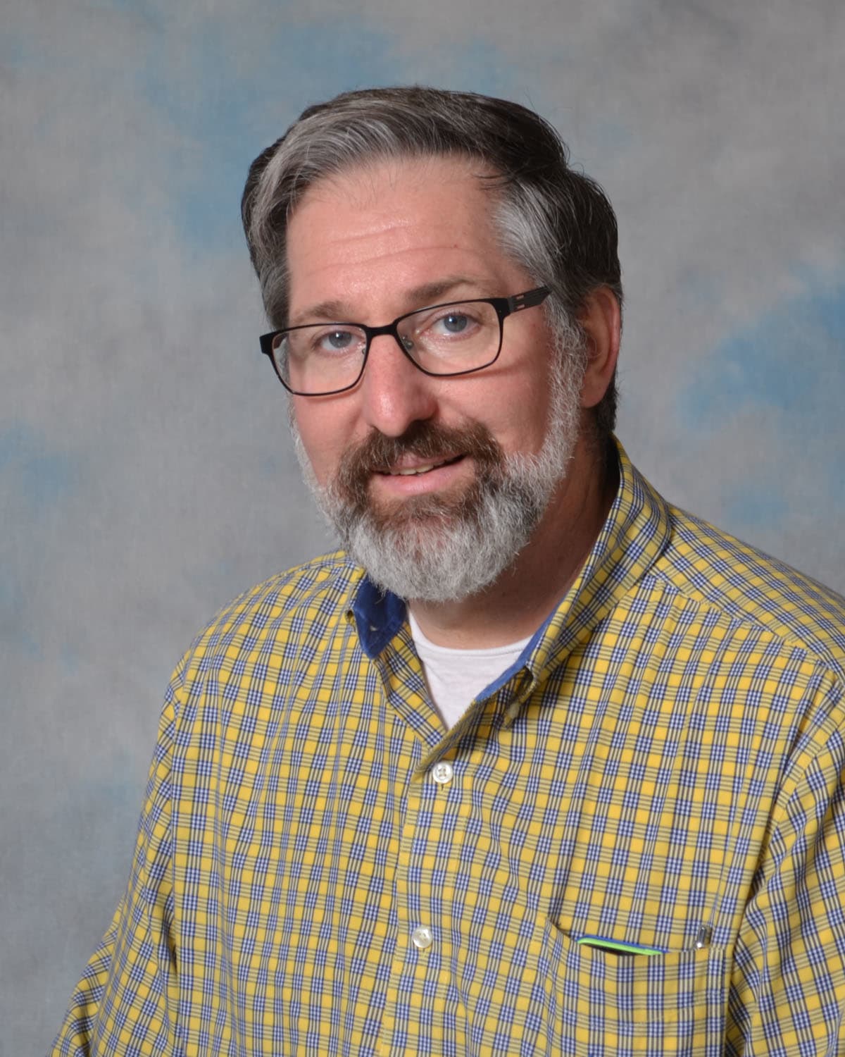 A person with dark hair wearing a blue shirtDescription automatically generated