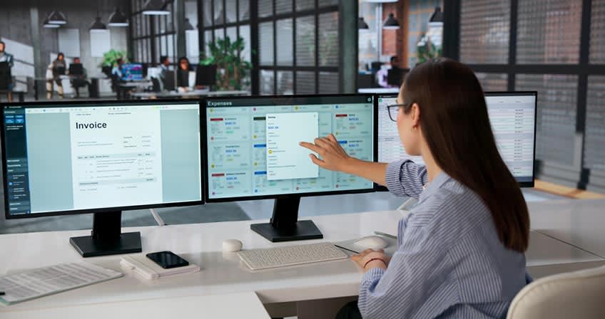 Young accountant analyzes invoice data with the help of AI across multiple computer screens at work