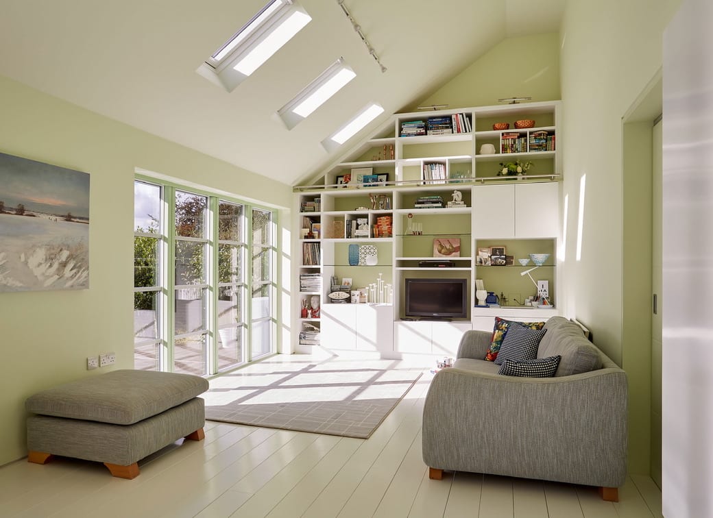 a custom-designed living room/study with a wall of windows, light green walls, and white built-in shelving