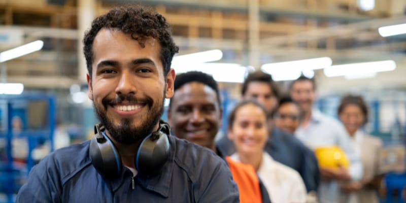 Team of workers at a factory standing in a row smiling at camera with arms crossed.