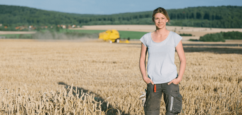 Farmer standing in a wheat field, combine harvester in the background
