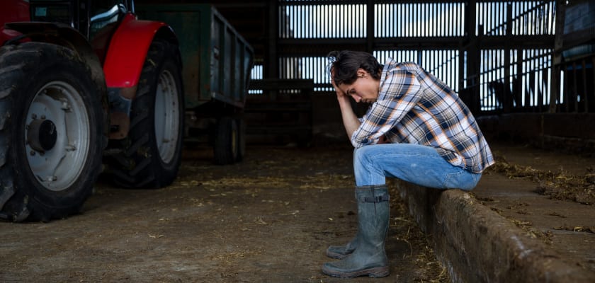 Upset farmer in barn sitting with their head in their hands.