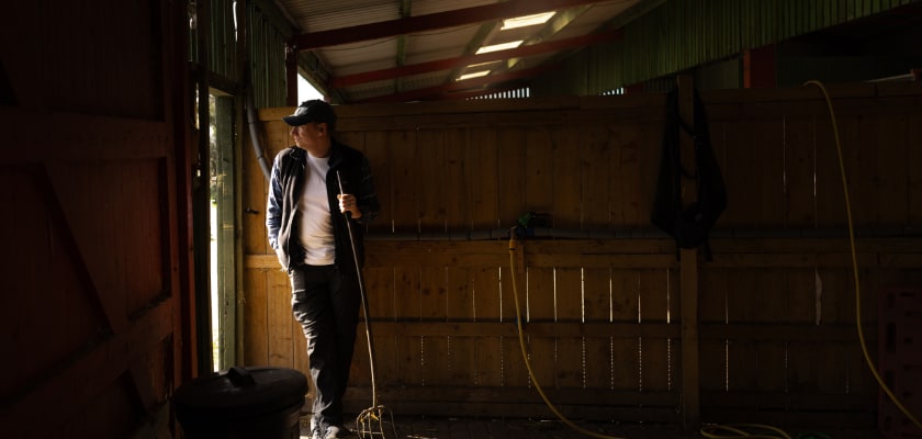 Farmer standing in a dark barn looking concerned.