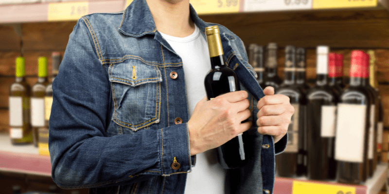 Man in a supermarket stealing a bottle of wine.