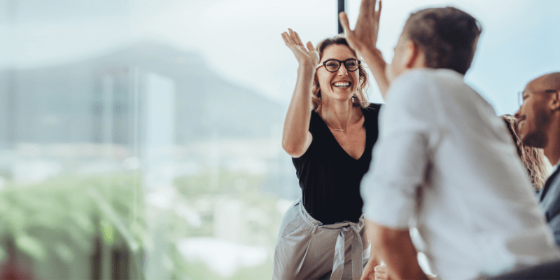Business professionals high five during a meeting in boardroom.