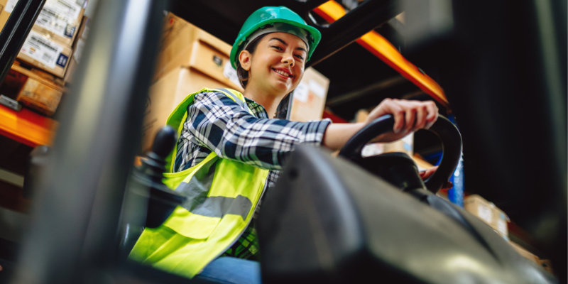 Female Forklift Driver Poses and Drives Worklift at Distribution Warehouse