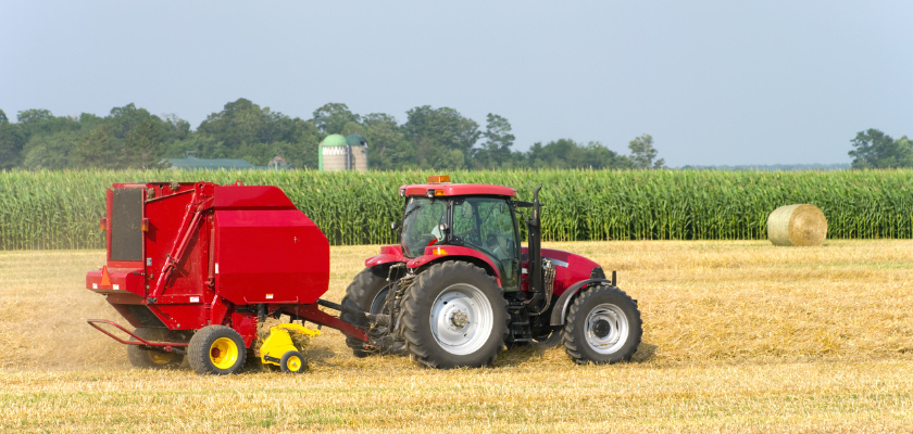 A large agricultural baler baling round bales of wheat straw.
