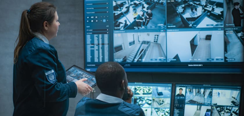 CCTV operators control security cameras on computer monitors and big digital screen with surveillance footage.