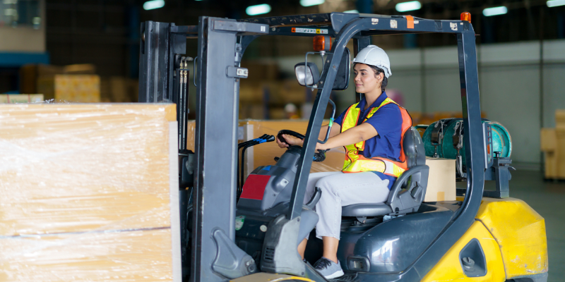 Worker moving items on a forklift in a warehouse.