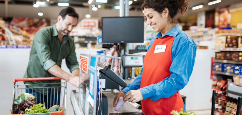 Employee at cash register in supermarket, serving a customer.