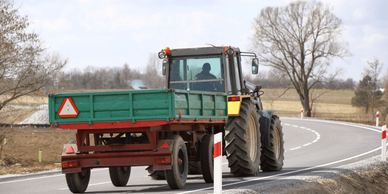 A photo of a tractor on a public road with a slow moving vehicle sign.