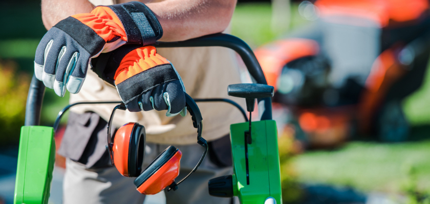 Photo of a landscaper wearing protetive gloves and holding hearing protection.