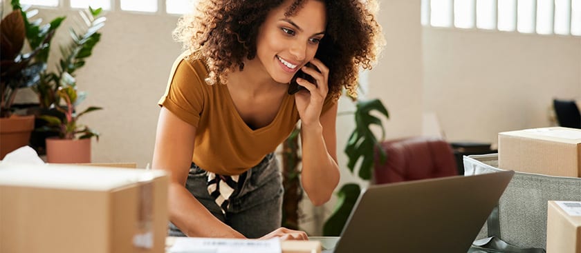 Person on the phone standing over desk using laptop