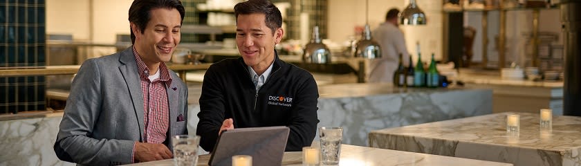Two professionals discussing business insights on a tablet in a restaurant setting.