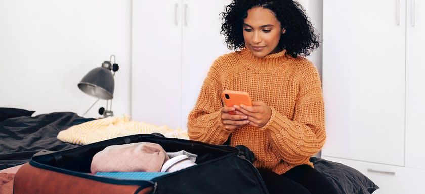 Woman packing suitcase and using phone for travel planning