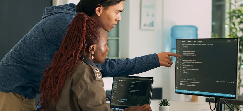 Two colleagues, one pointing at code on a computer screen, collaborating on software development