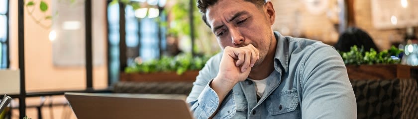 A man looking thoughtfully at his laptop, with his hand to his mouth, possibly contemplating a problem or decision.