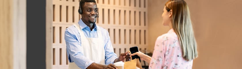 Coffee shop employee handing bag and cup to customer at checkout counter