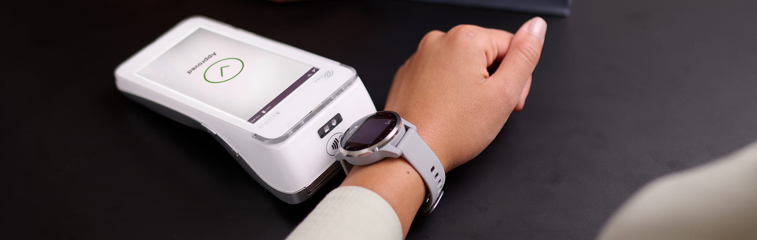 Close-up of a person using a smartwatch for a contactless payment at a point-of-sale terminal.
