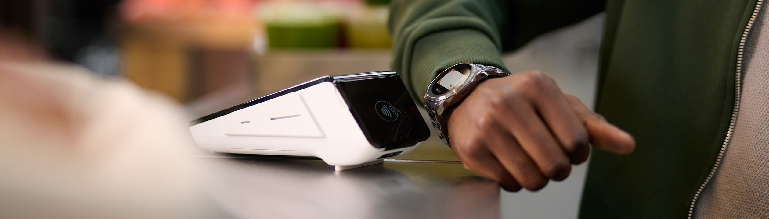 Person making a contactless payment at a point-of-sale terminal using a smartwatch wearable device.