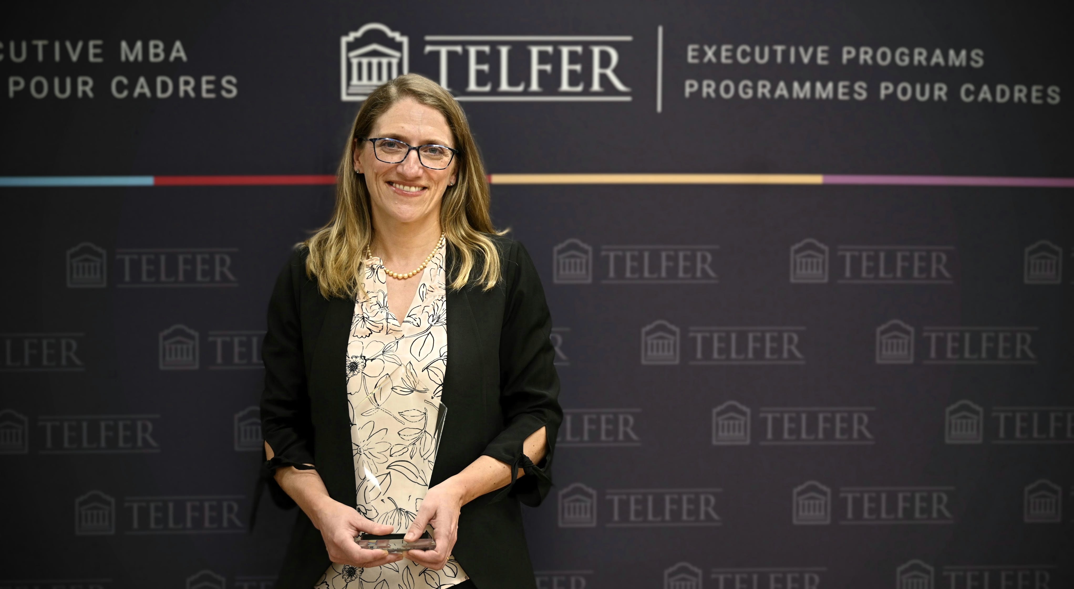 Une femme (la Dre Tammy LeRiche) debout devant un fond noir avec son Prix d’excellence de Telfer pour le leadership en amélioration des soins de santé.