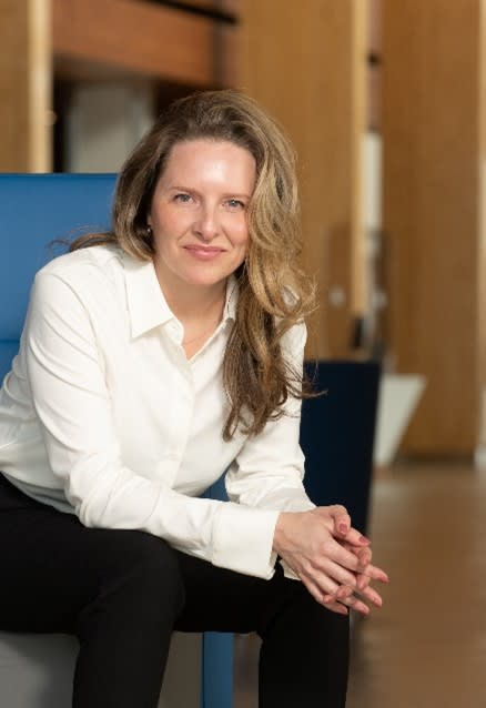 Elizabeth Tanguay wearing a white blouse and black slacks, sitting down and smiling at the camera for a headshot.