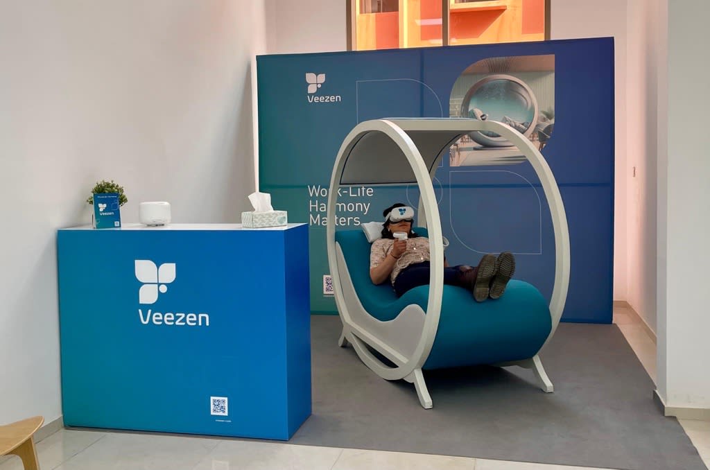 Person in a modern relaxation pod with VR headset at a branded Veezen booth.