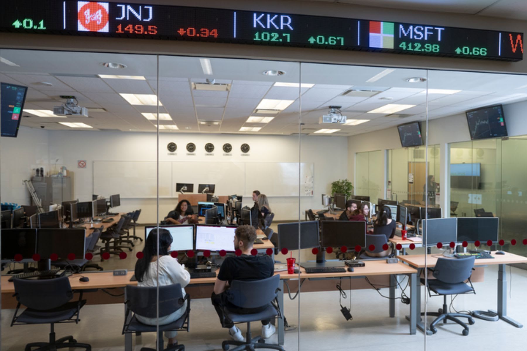 Des étudiantes et étudiants du-B.Com. travaillent devant les ordinateurs du Laboratoire de recherche et d’apprentissage en finance de l’École de gestion Telfer. Photo de l’intérieur du laboratoire prise de l’extérieur de l’enceinte vitrée.