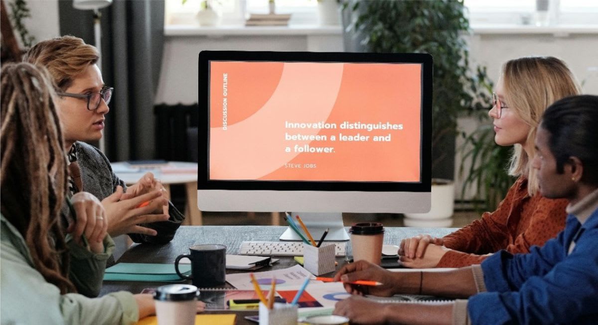 Unidentified group of people having a discussion at a table with a computer monitor at the center that reads Innovation distinguishes between a leader and a follower.