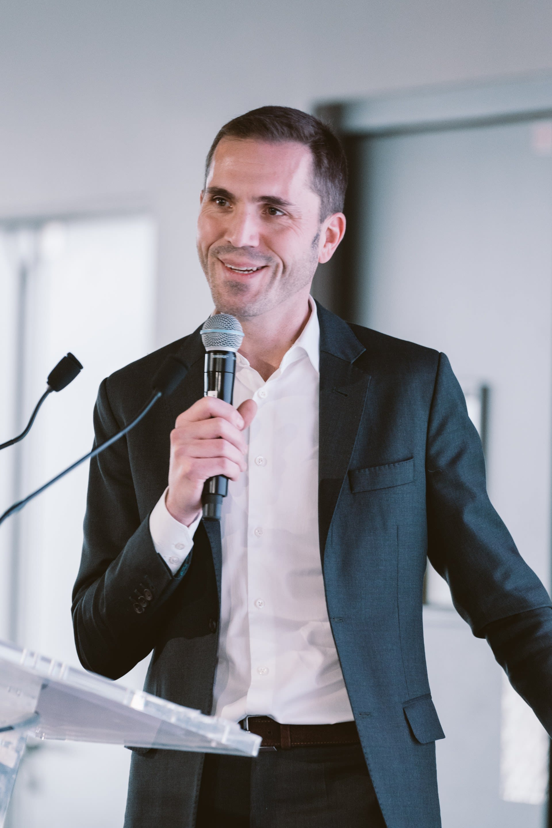 Arnaud Sabadie holding a microphone at a podium.