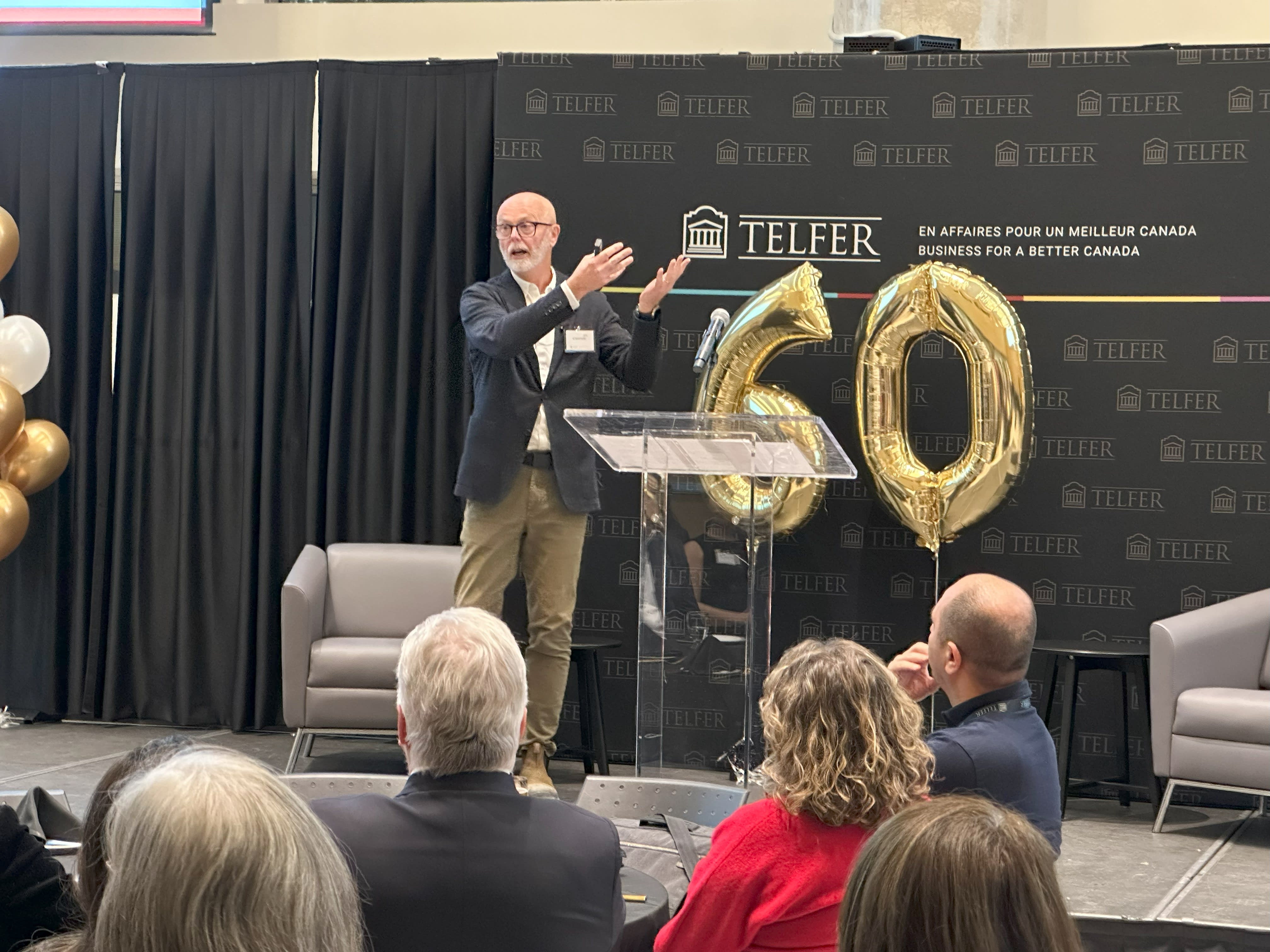 Micheal speaking in front of a crowd and the numbers 60 behind him