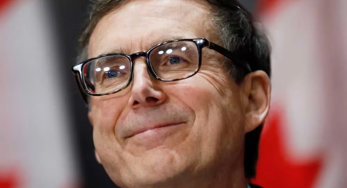 Tiff Macklem, Governor of the Bank of Canada, smiling during a formal event with Canadian flags in the background.