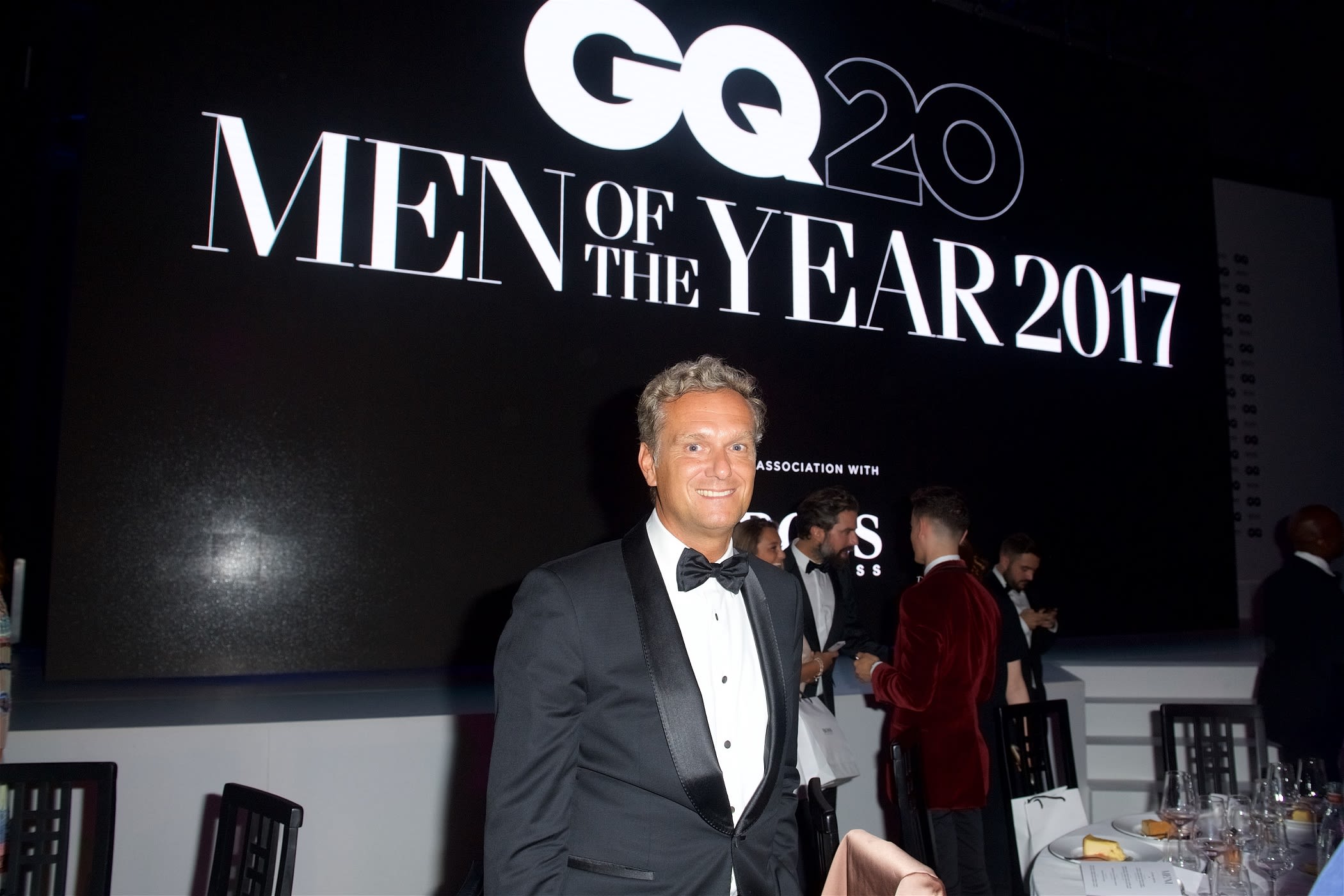 Stephan Born in a tuxedo poses in front of a GQ Men of the Year sign.