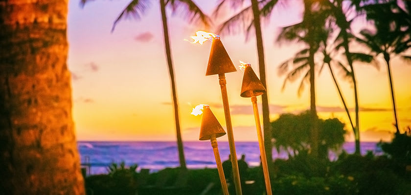 tiki lights in front of an ocean with the sunset