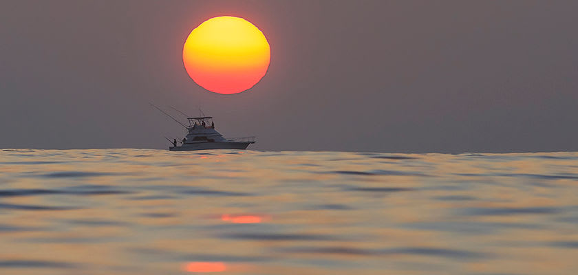 deep sea fishing boat in ocean with sunset behind