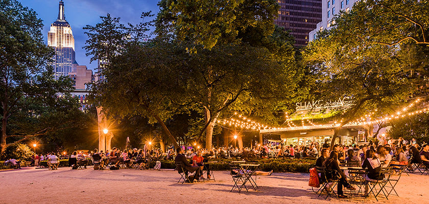 People sitting outside La Grande Boucherie restaurant in evening with view of Empire State Building in distance