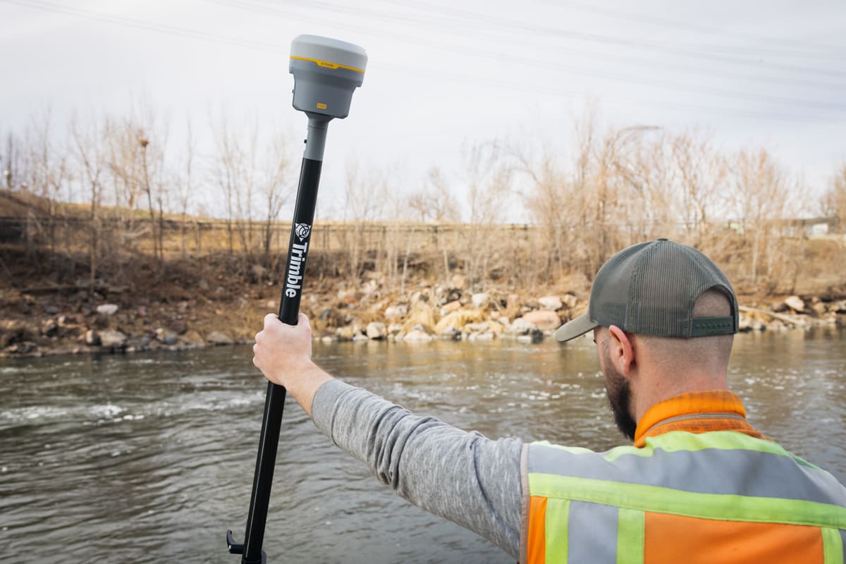 Surveyor standing beside a river holding a survey pole with the Trimble R980