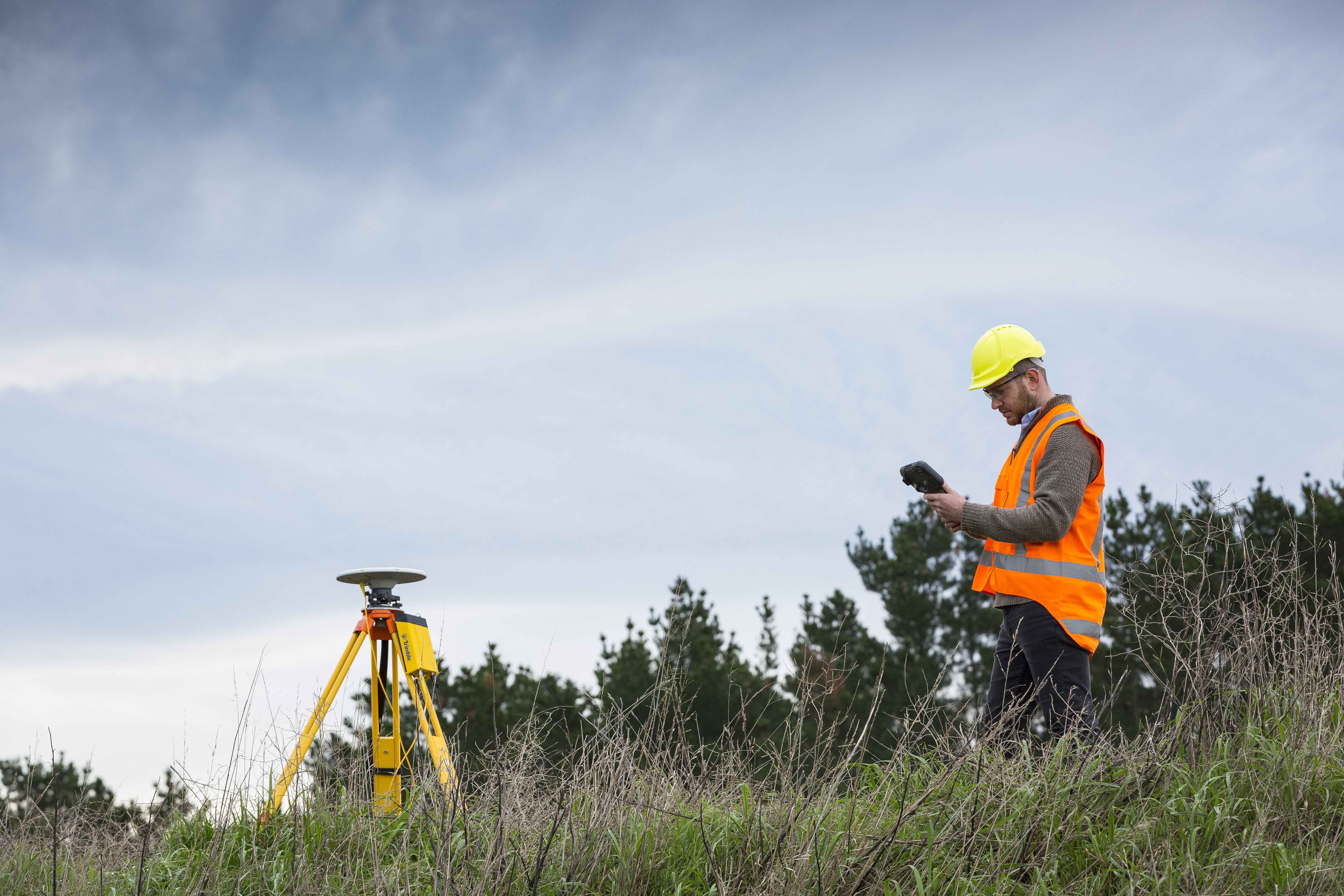 Surveyor in rural setting standing near a base station set up on tripod