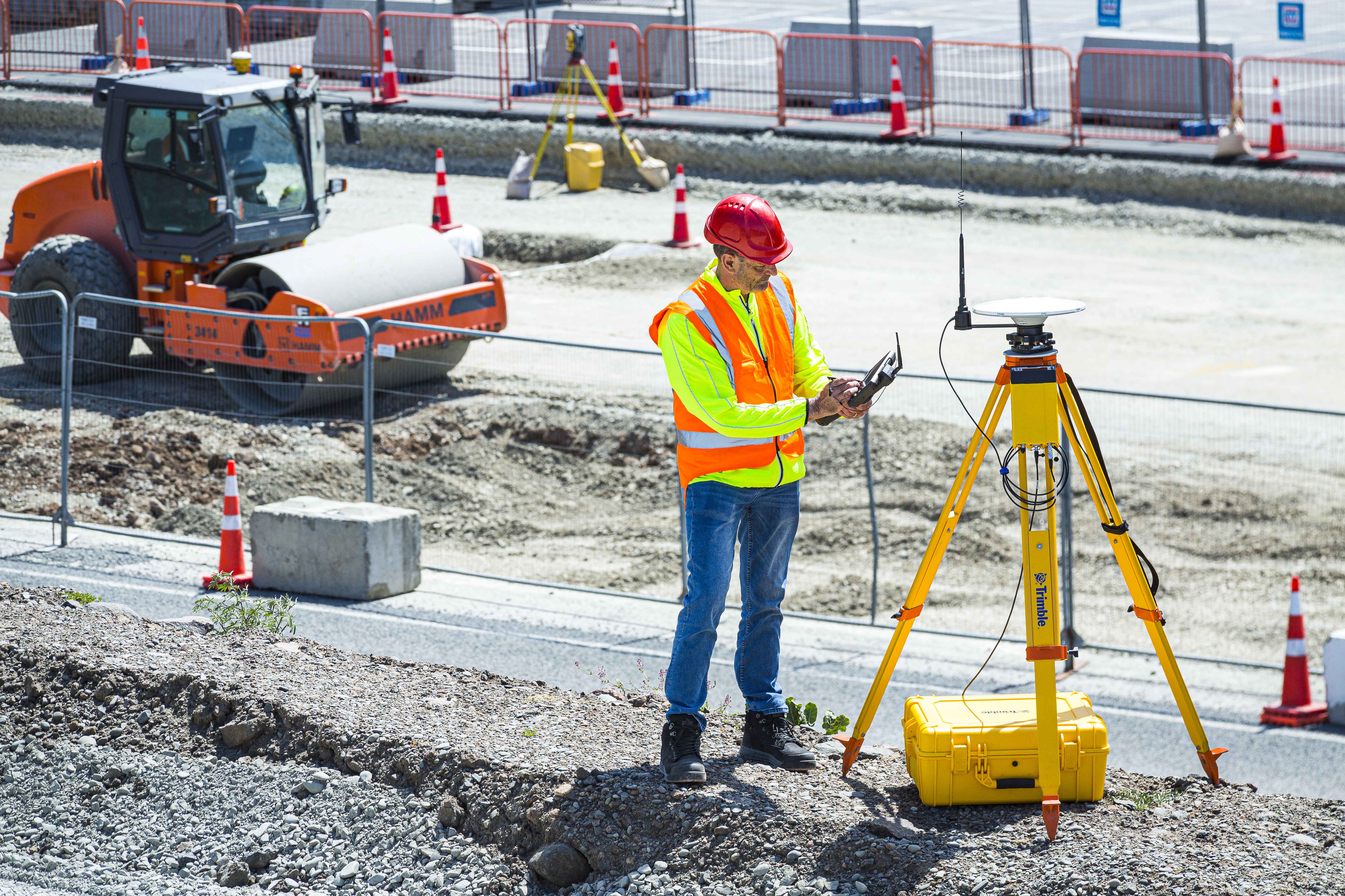 A surveyor on a construction site standing beside the Trimble R750 Model 2 as a base station
