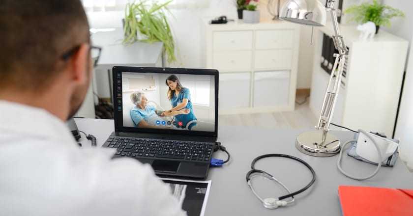 Doctor watching a nurse with a client on his laptop