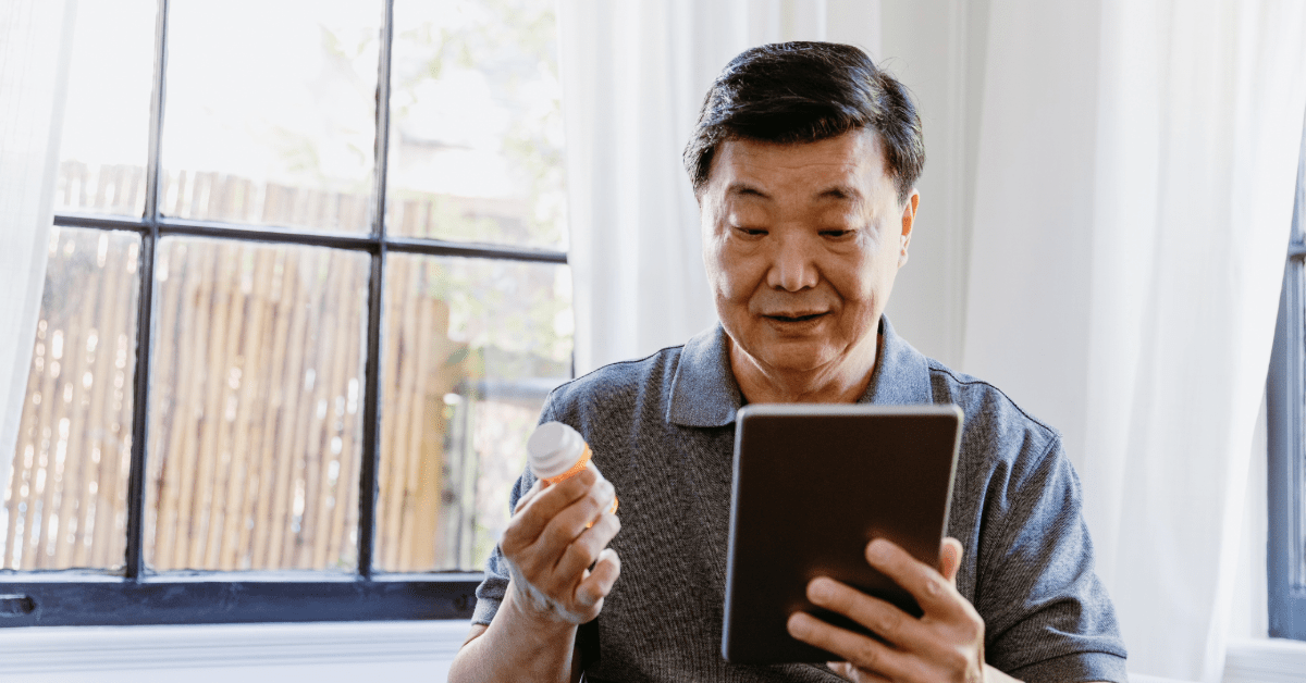 An older man looking down at a prescription bottle while holding a computer tablet
