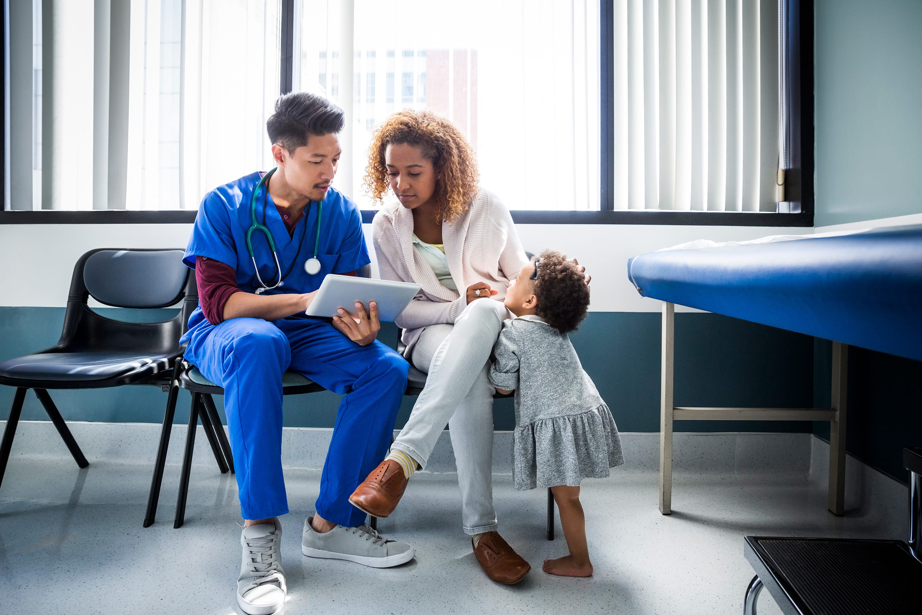 A doctor and a woman looking at a tablet while a child is reaching for the woman